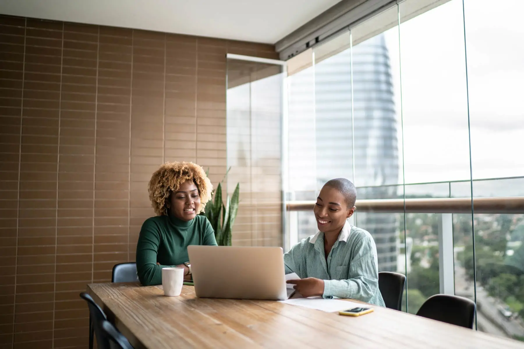 Two female business colleagues looking at laptop in a conference room.