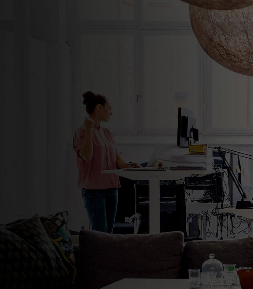 A woman working at a standing desk in an open office.