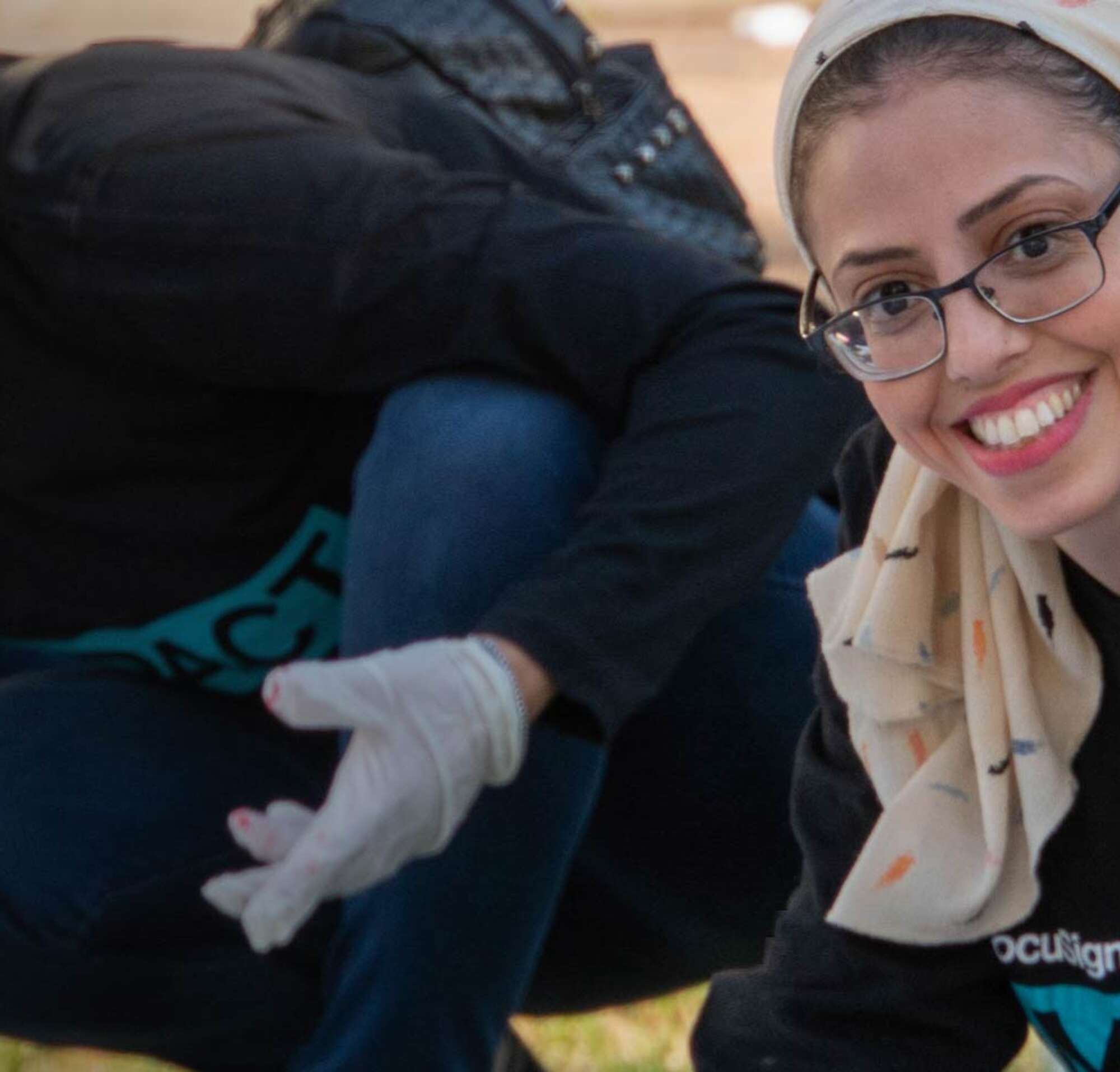 A smiling woman wearing a DocuSign IMPACT t-shirt and a headscarf, volunteering in the community