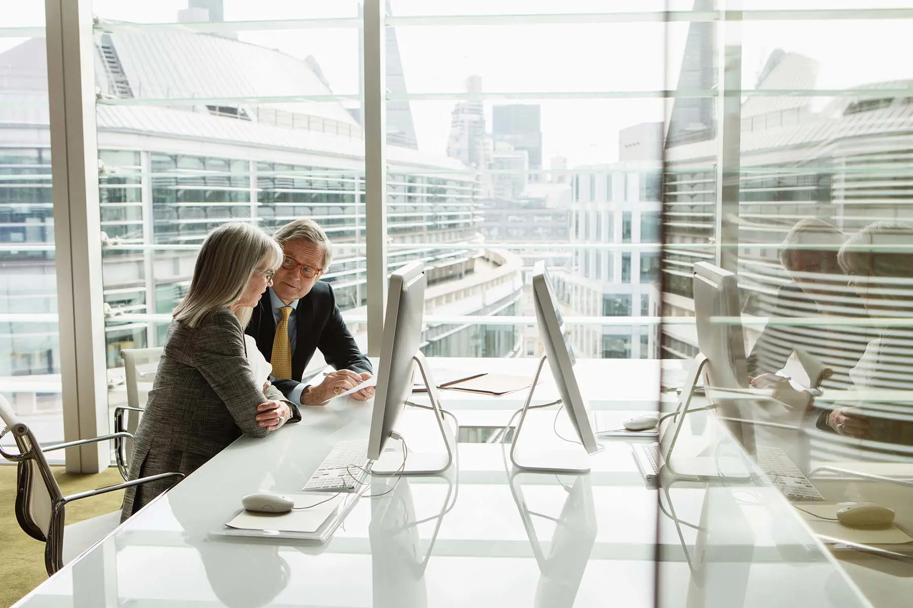 Two employees having a discussion in an office with glass windows.