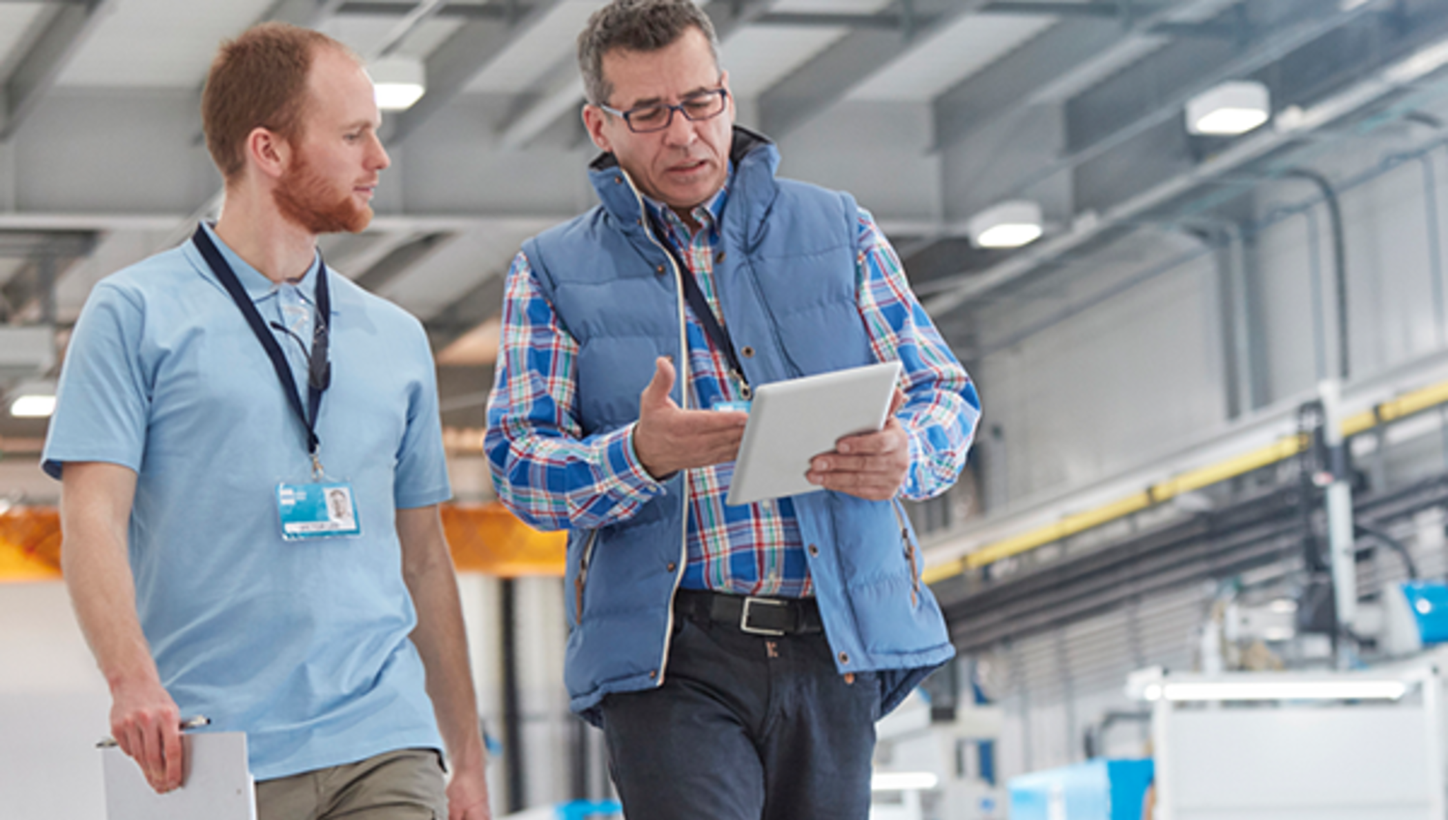 Two men walking in a warehouse with a tablet.